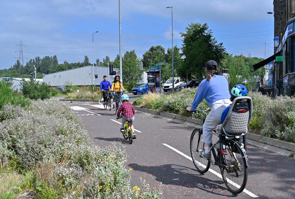 People cycling on a protected cycle lane on Garscube Road in the north of Glasgow, including mother cycling with her two children.